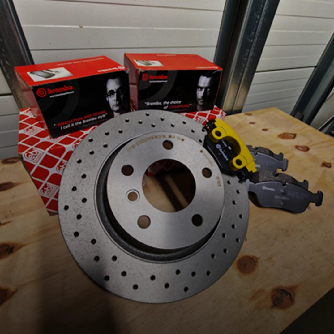 Complete Brembo en Febi Bilstein remmenupgrade set met geperforeerde remschijf en remblokken op een houten tafel.