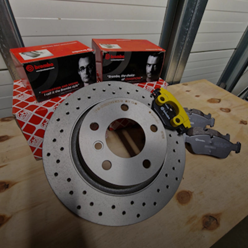 Nieuwe Brembo remmenset met een geperforeerde sportremschijf, Brembo remblokken en een Febi Bilstein onderdelendoos op een werkbank.